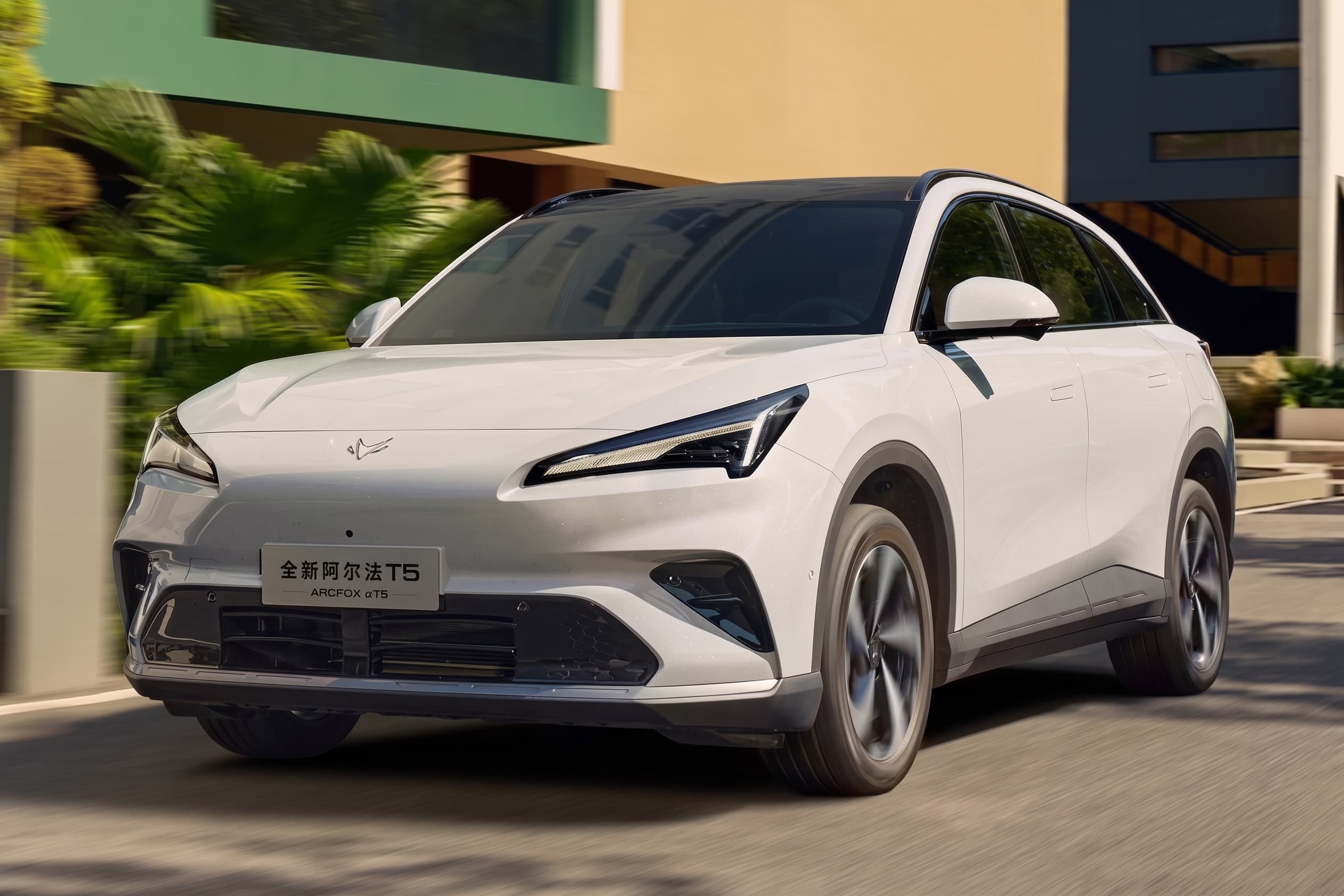 SUV branco em movimento numa via urbana, visto de três quartos dianteiro, com prédios e vegetação ao fundo