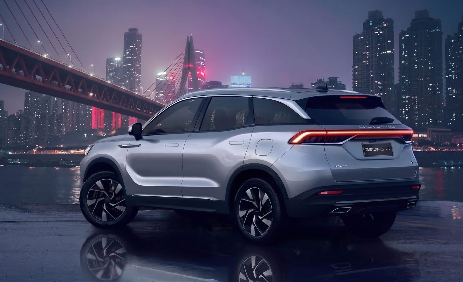 BAIC X7 prata visto de três quartos traseiro, com uma ponte iluminada ao fundo